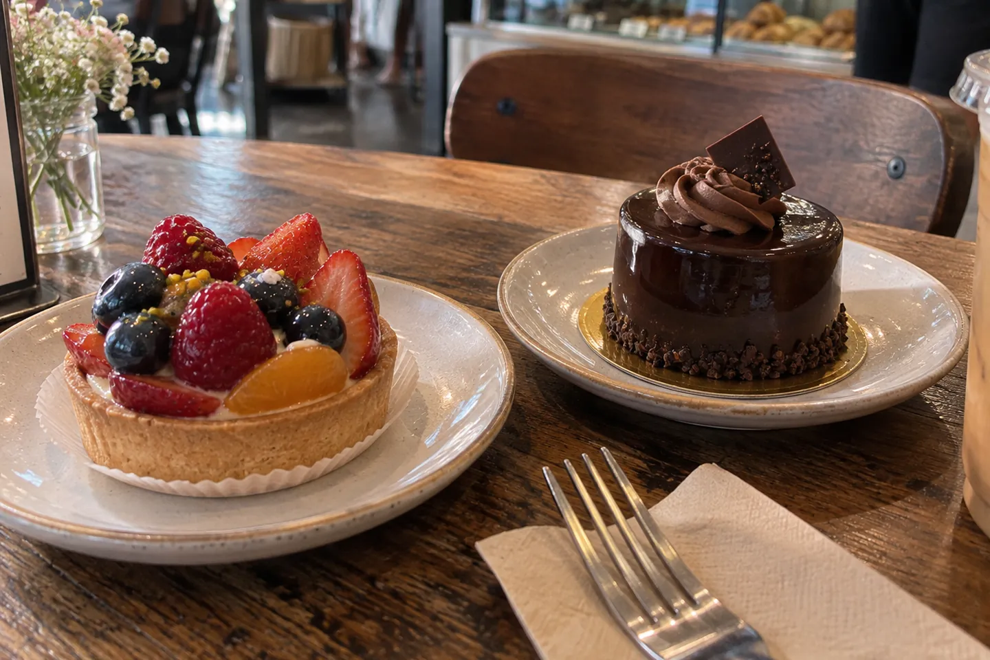 Fruit tart and chocolate cake on plates at a bakery table