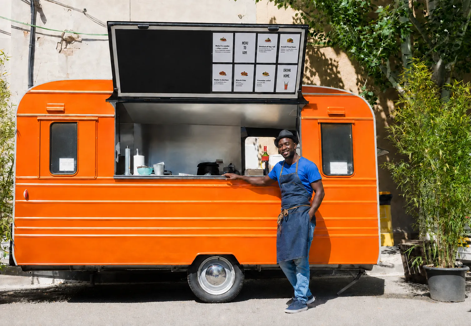 Owner standing beside an orange food truck with the service window open