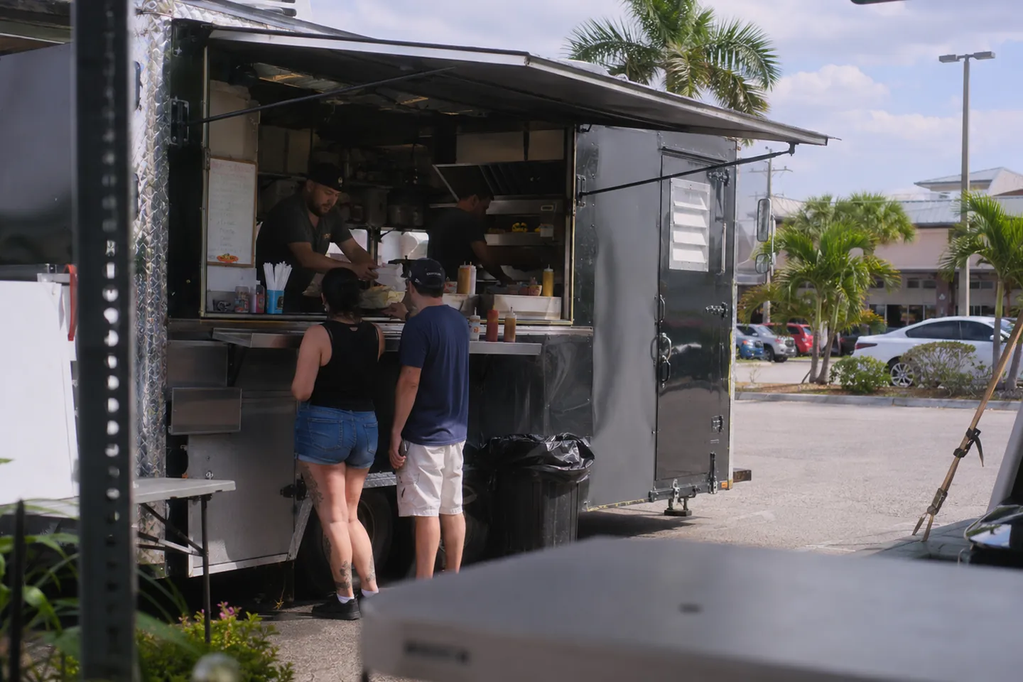 Customers ordering at a food truck window with the menu board open