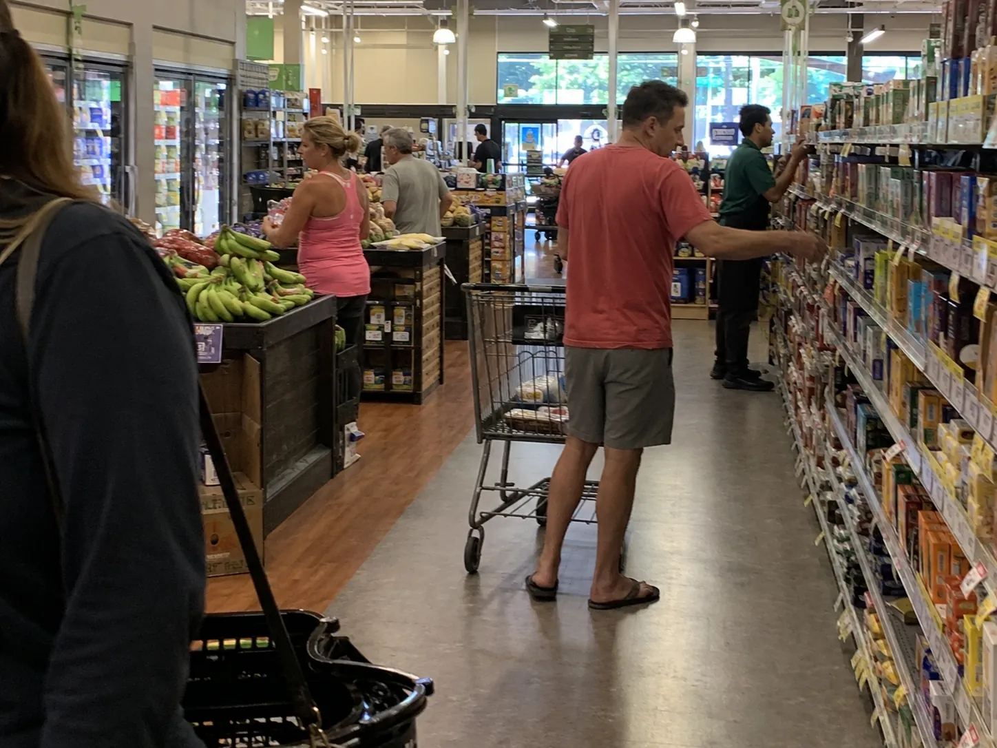 Grocery store aisle with shoppers, a produce display, and a shopping cart