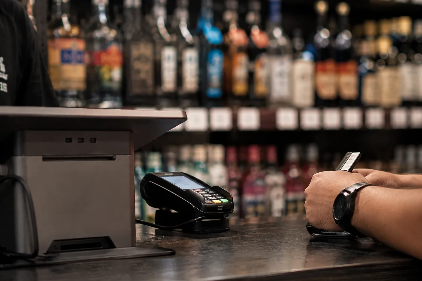 Customer holding a card next to a payment terminal on a liquor store counter