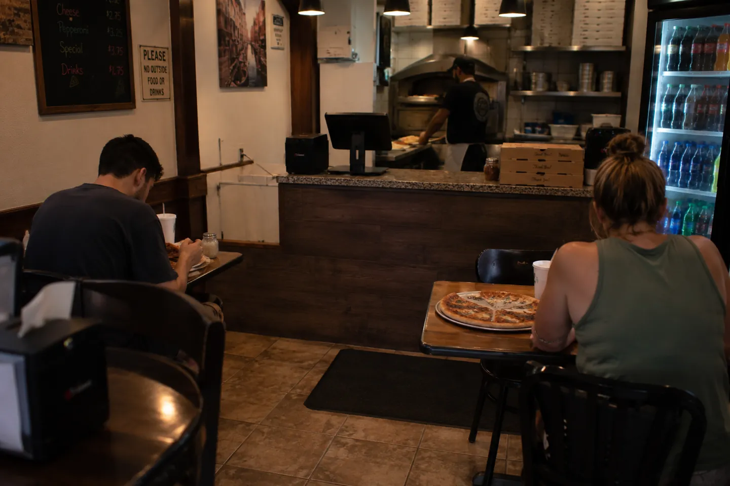 Pizzeria counter with a register, stacked pizza boxes, and the oven behind