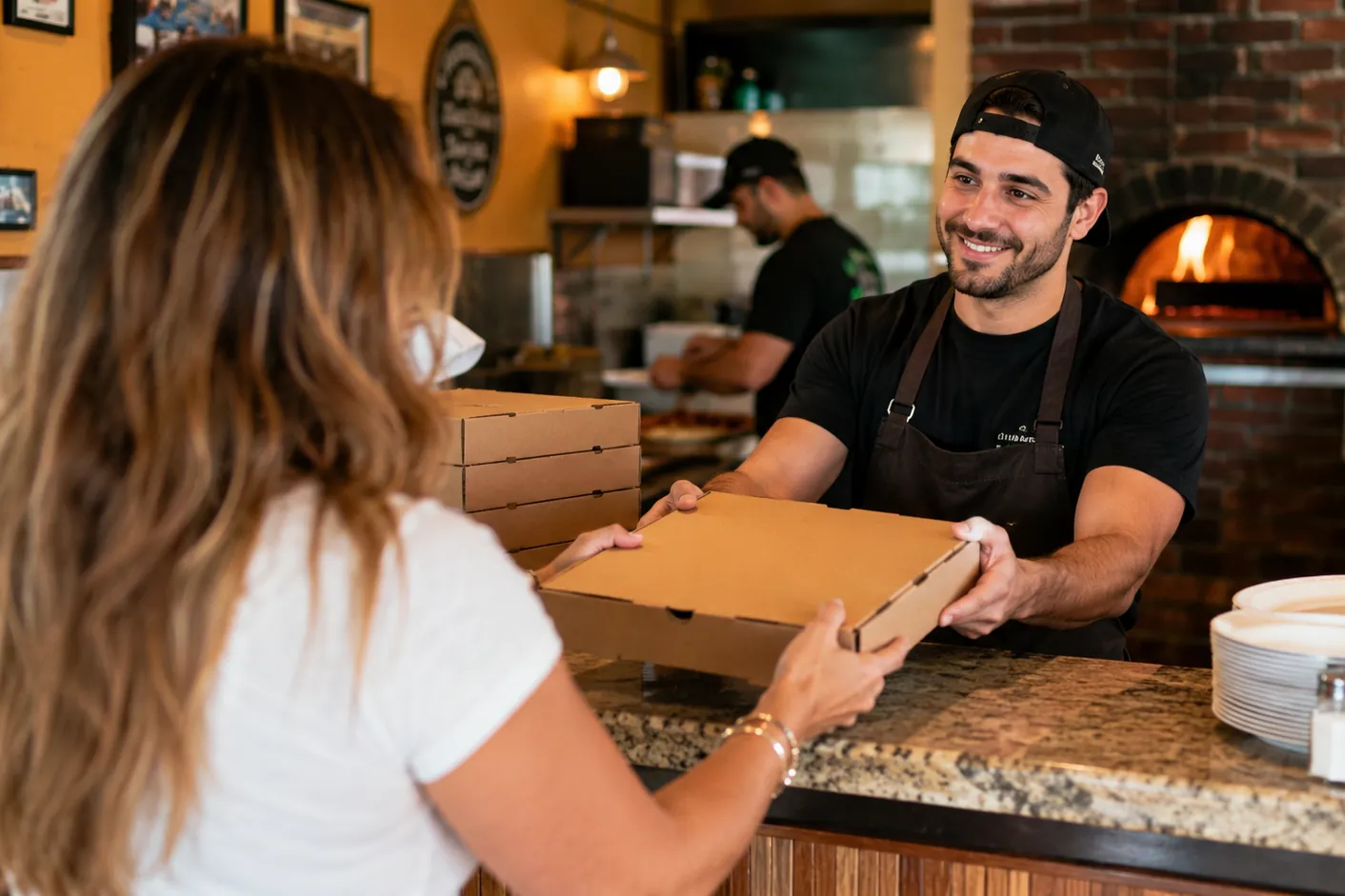 Staff member handing a pizza box to a customer at the pickup counter