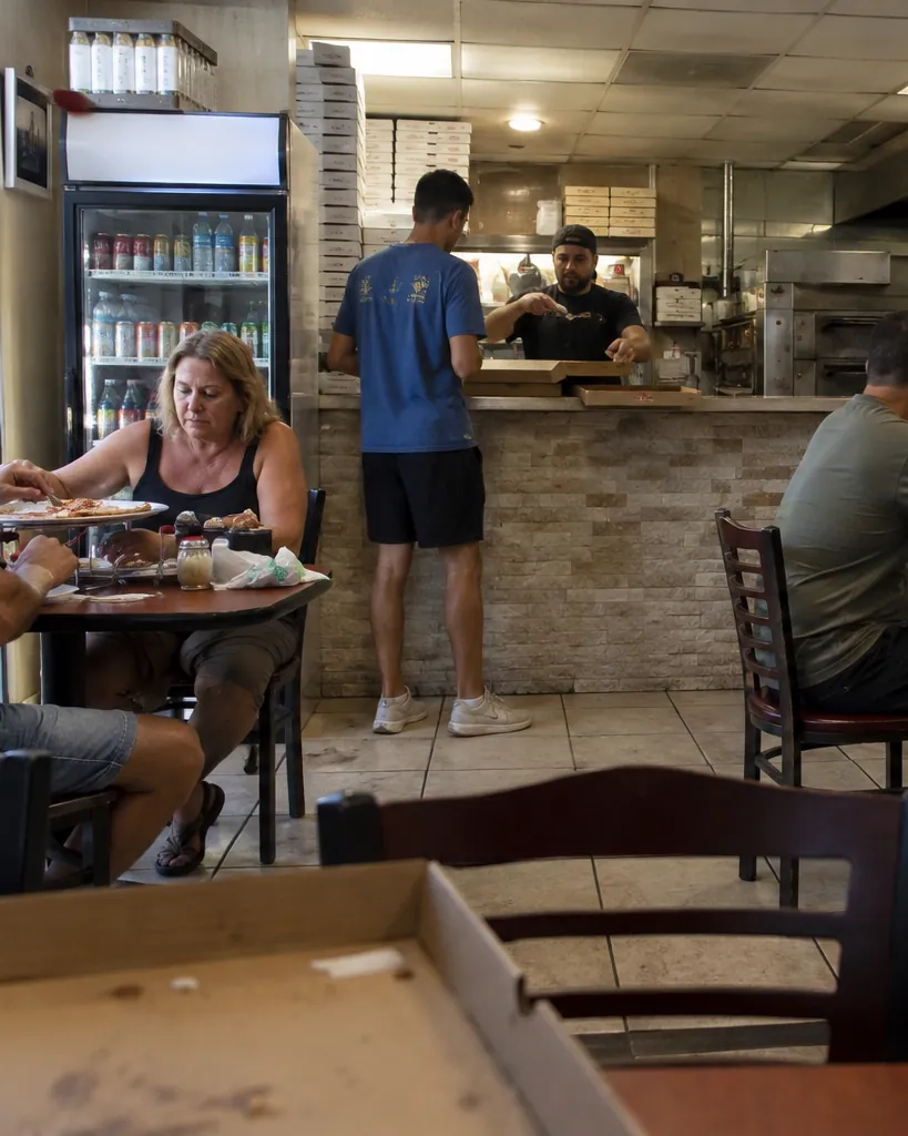 Cliente recogiendo una caja de pizza en el mostrador mientras los comensales comen en las mesas